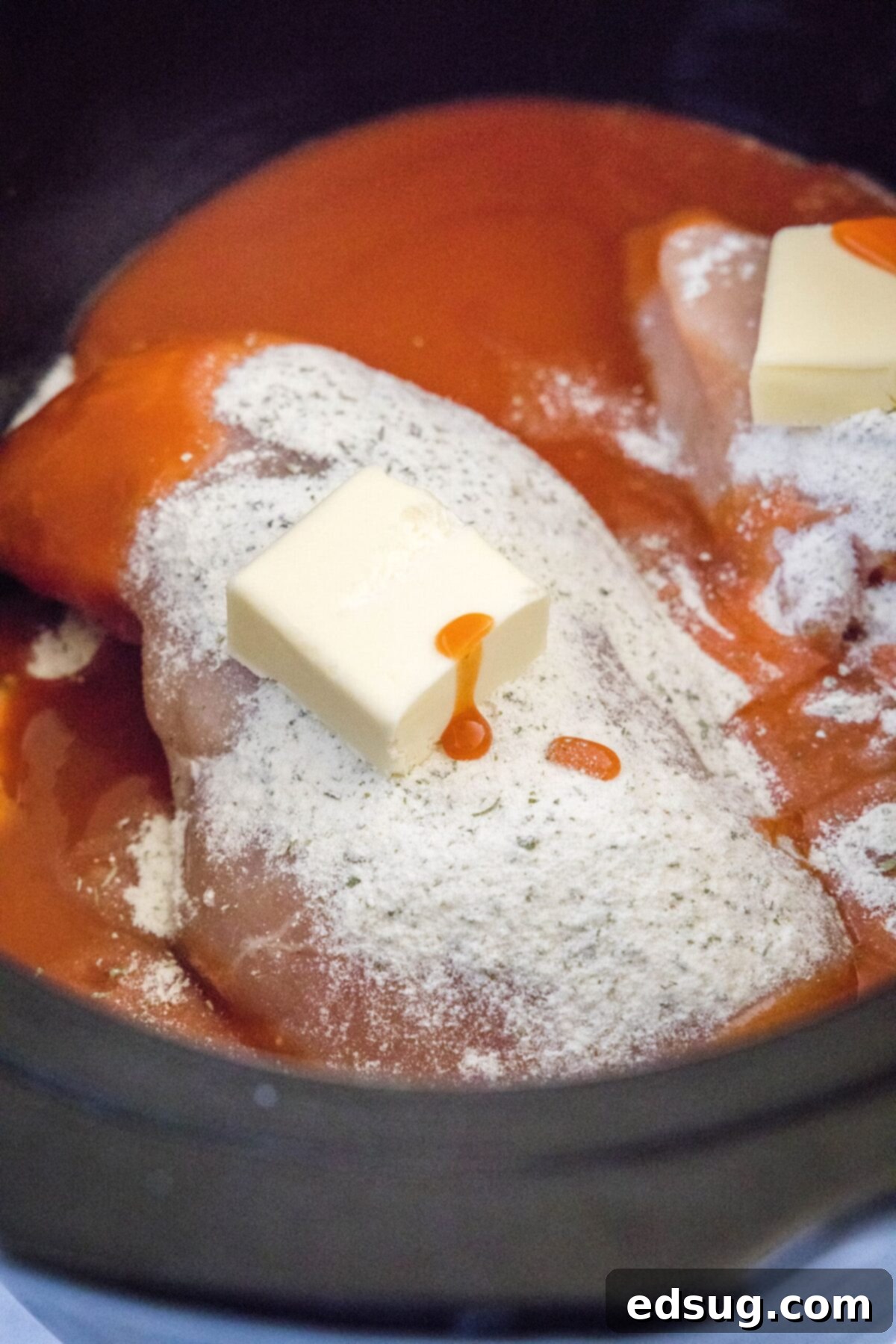 Chicken breasts in a slow cooker topped with ranch dressing mix, buffalo sauce, and butter
