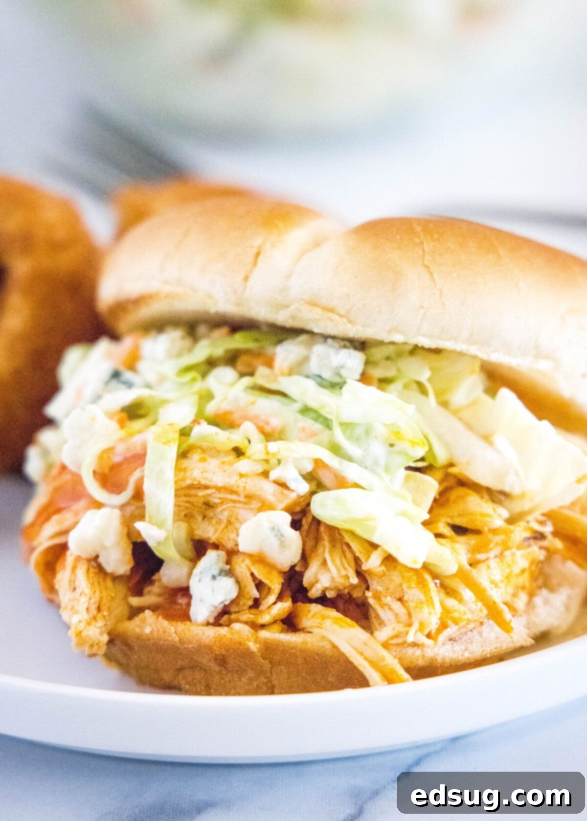 Close up of a buffalo chicken sandwich topped with coleslaw and blue cheese