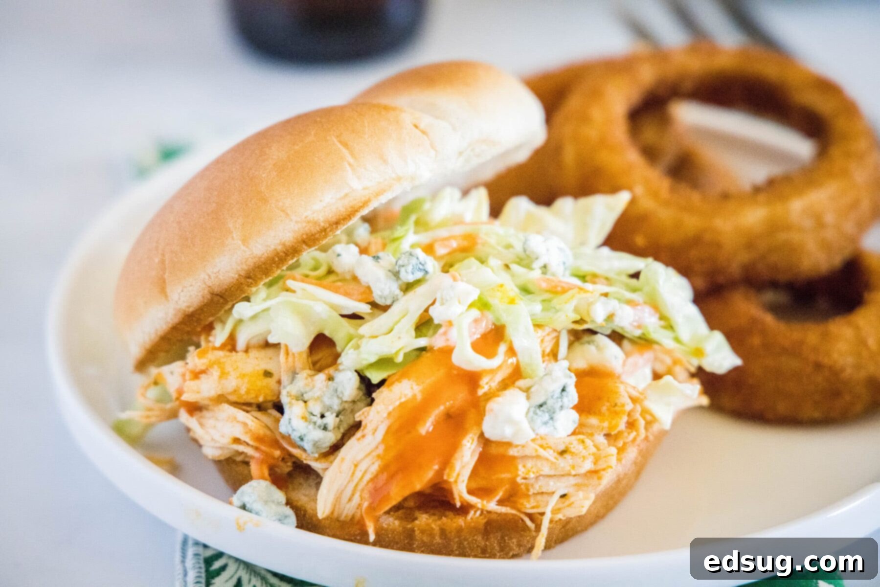 A plate with a buffalo chicken sandwich and onion rings on it