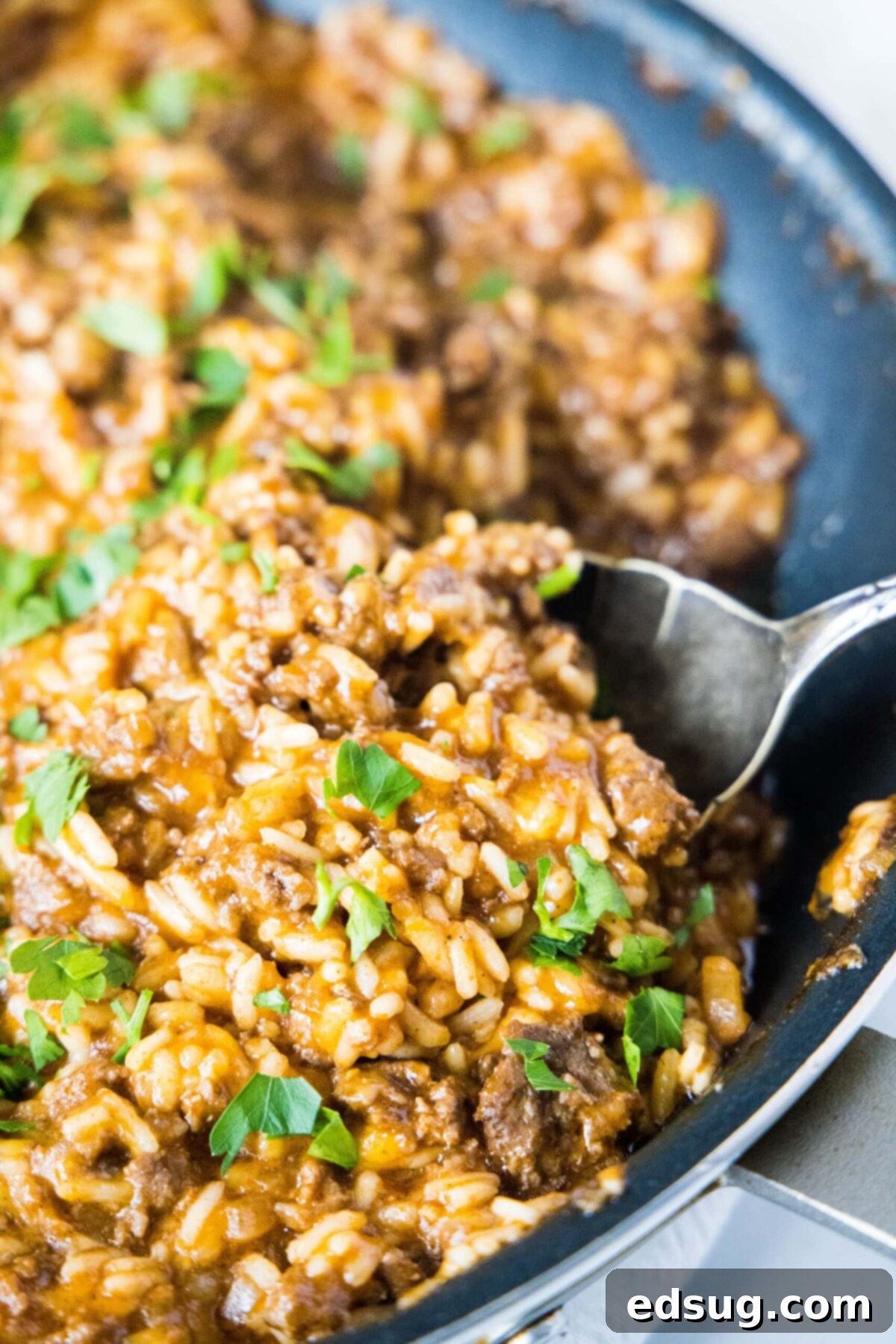 Close up of a spoon taking a spoonful of beefy taco rice out of a skillet