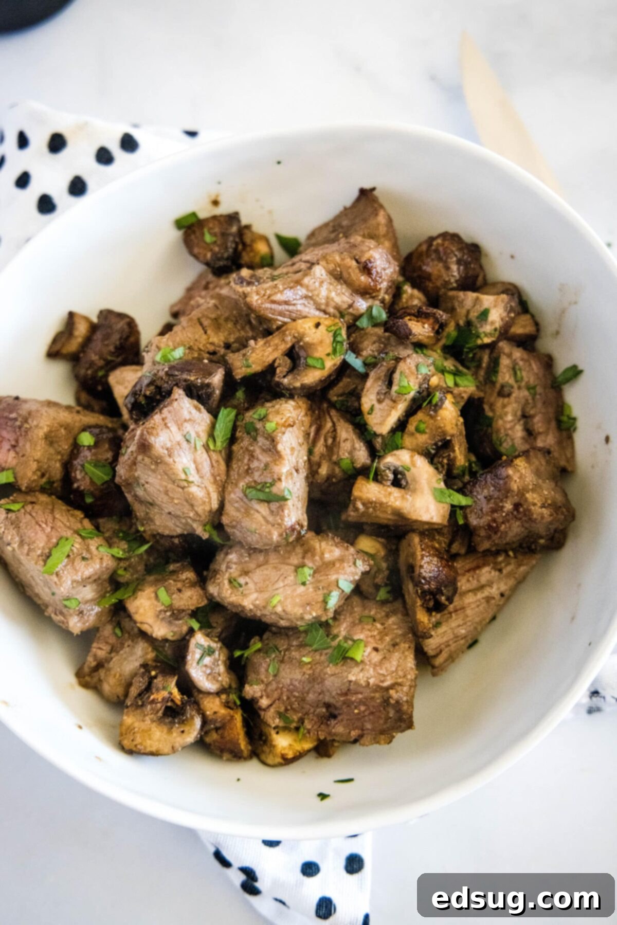 How to make easy air fryer steak bites with mushrooms and garlic powder, with tender meat and juicy mushrooms. It only takes 15 minutes! An inviting overhead view of a rustic serving bowl filled to the brim with perfectly cooked, tender, and juicy air fryer steak and mushroom bites, ready to be enjoyed.