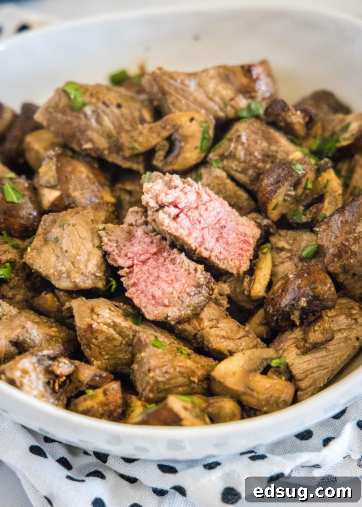 How to make easy air fryer steak bites with mushrooms and garlic powder, with tender meat and juicy mushrooms. It only takes 15 minutes! A beautifully presented serving bowl filled with succulent air fryer steak and mushroom bites, with one of the steak pieces thoughtfully cut in half to showcase its perfectly medium-rare, juicy interior.