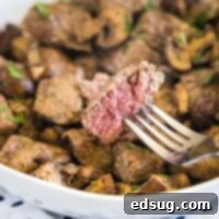 A piece of steak on a fork with a plate of steak and mushroom bites in the background