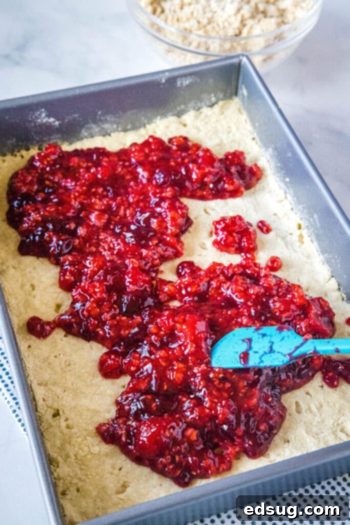 Luscious Raspberry Crumble Bars 4 spreading raspberry filling over partially baked shortbread crust in a baking pan