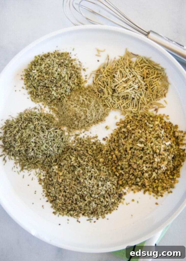 A pristine white plate holds six distinct piles of dried herbs: basil, thyme, oregano, marjoram, rosemary, and sage, showcasing the individual components of Italian seasoning.