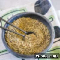 A bowl of Italian seasoning with a spoon in it, on top of a kitchen towel