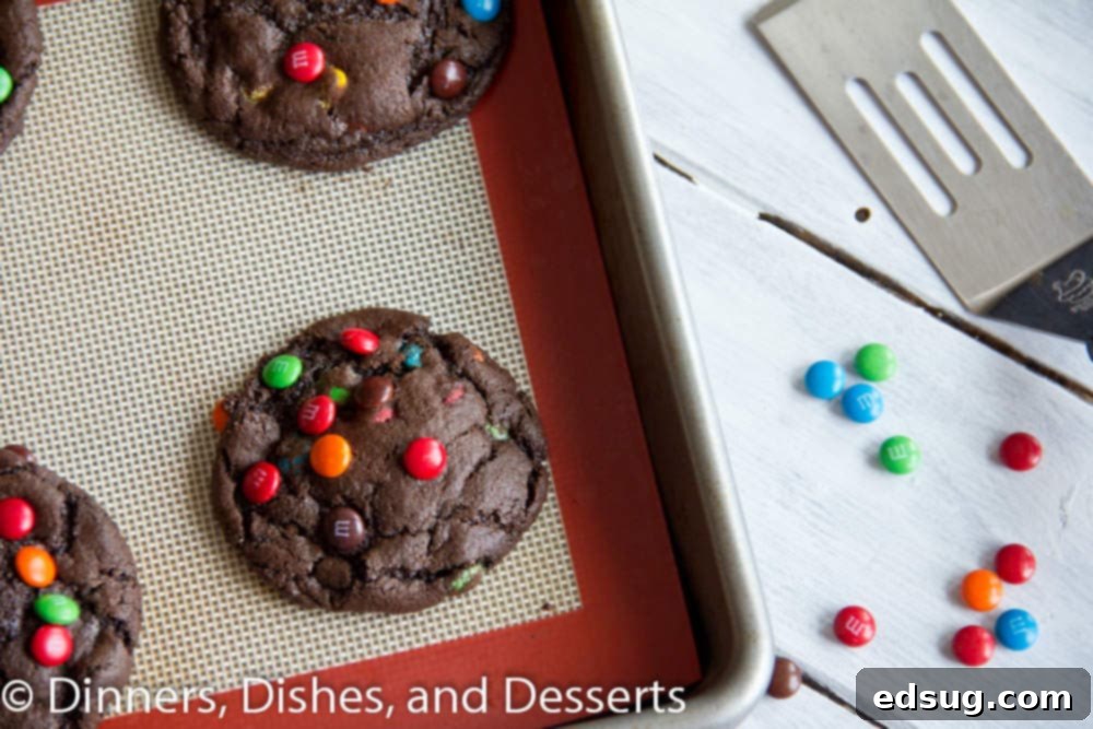 Best Chewy M&M Chocolate Cookies Batch of chocolate M&M cookies on a baking sheet, ready to be cooled