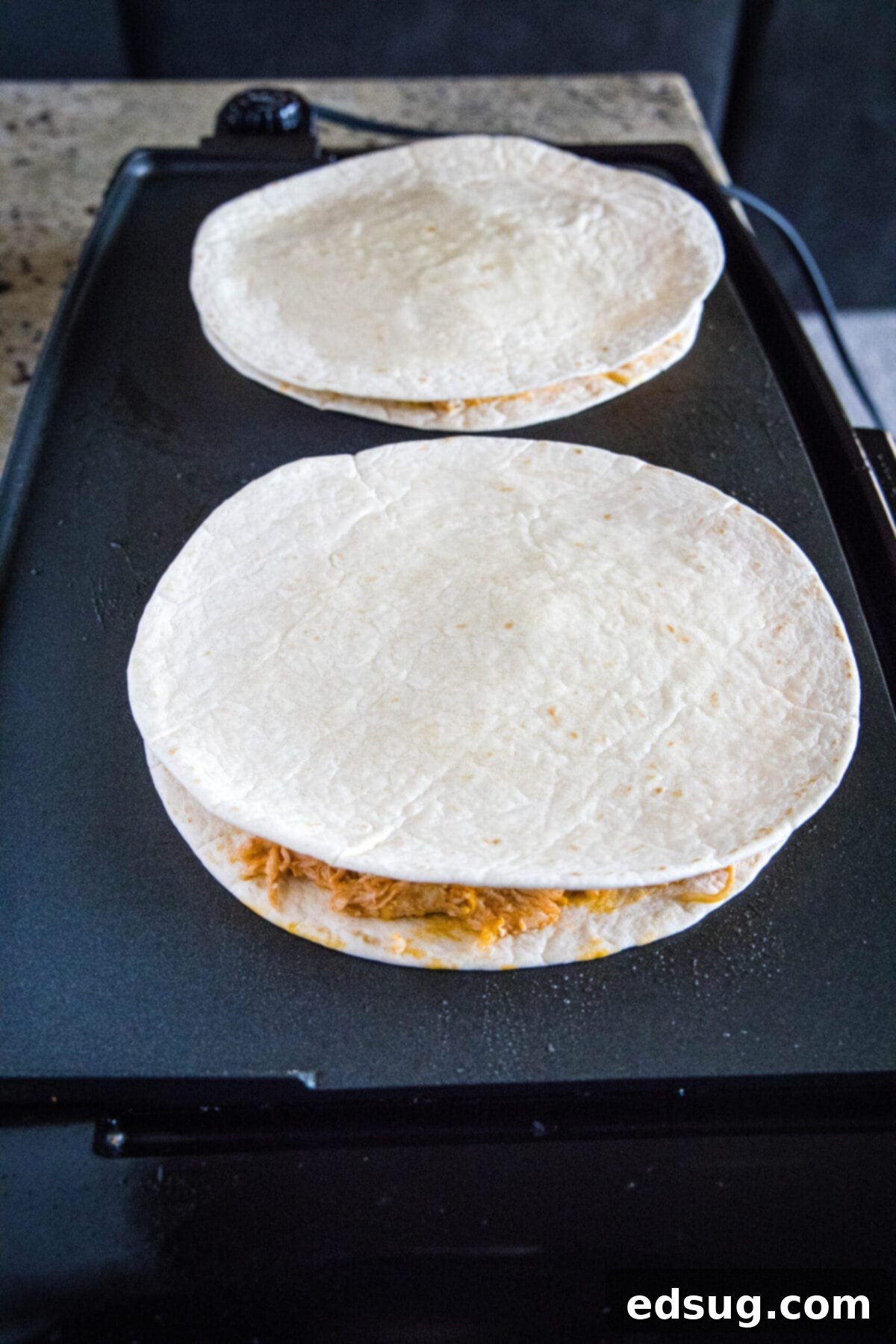 This easy homemade buffalo chicken quesadilla recipe is loaded with juicy chicken, melty cheese, and spicy wing sauce. Two uncooked quesadillas on a skillet
