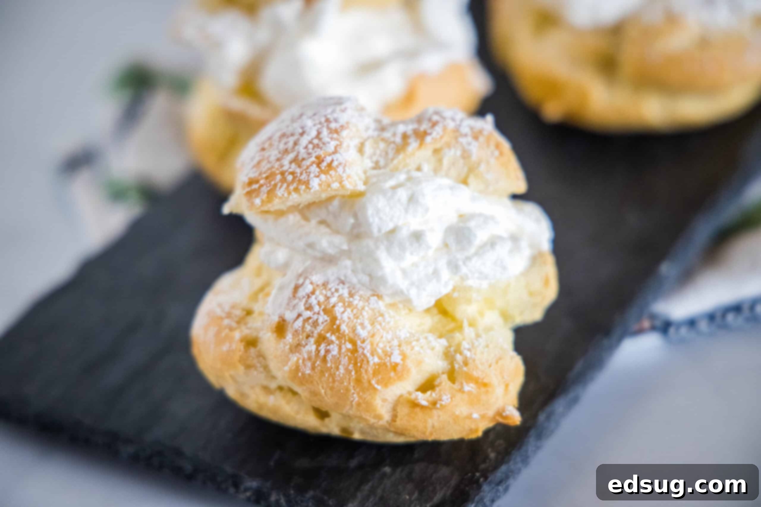 A platter of gorgeous homemade cream puffs, elegantly dusted with powdered sugar, ready to delight guests. A beautiful platter filled with numerous homemade cream puffs, each dusted generously with powdered sugar, ready for serving.