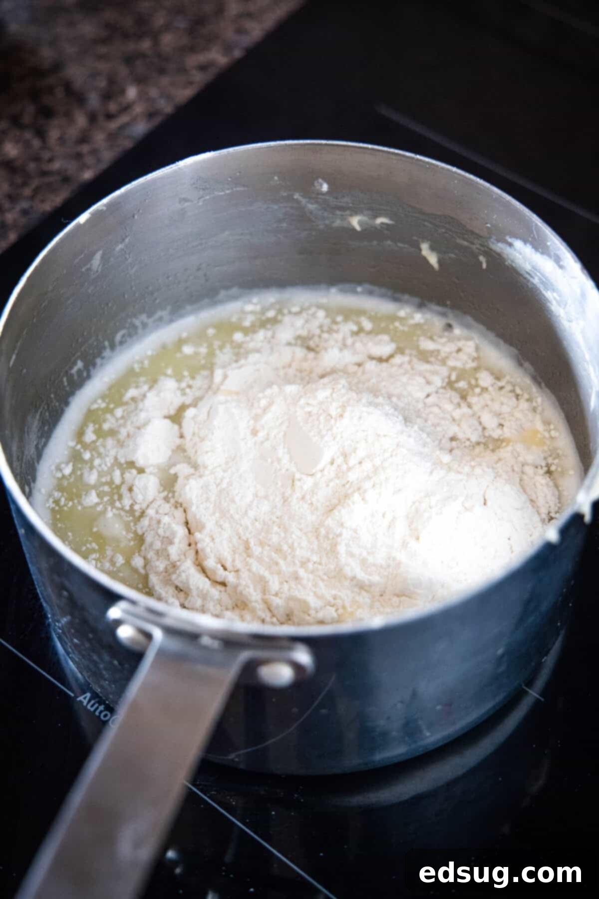 Combine water and butter, then add flour to create the choux pastry base. Flour being added to melted butter and boiling water in a saucepan on the stovetop.