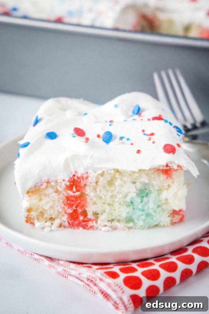 Close up slice of 4th of July poke cake showing red and blue jello infused into the white cake with whipped cream on top