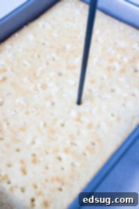 Using a chopstick to poke holes evenly across the top of a baked white cake