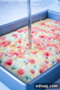 A straw being used to carefully add blue Jell-O into pre-poked holes on a white cake