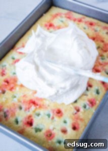 Spreading smooth, white whipped cream over the Jell-O infused poke cake for the final topping