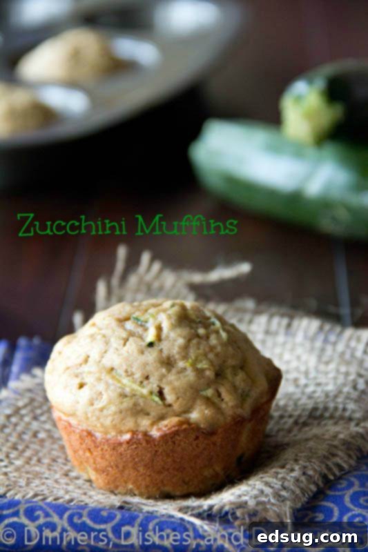 Close-up of freshly baked zucchini muffins on a rustic napkin, highlighting their golden brown tops and a hint of green flecks from the zucchini.