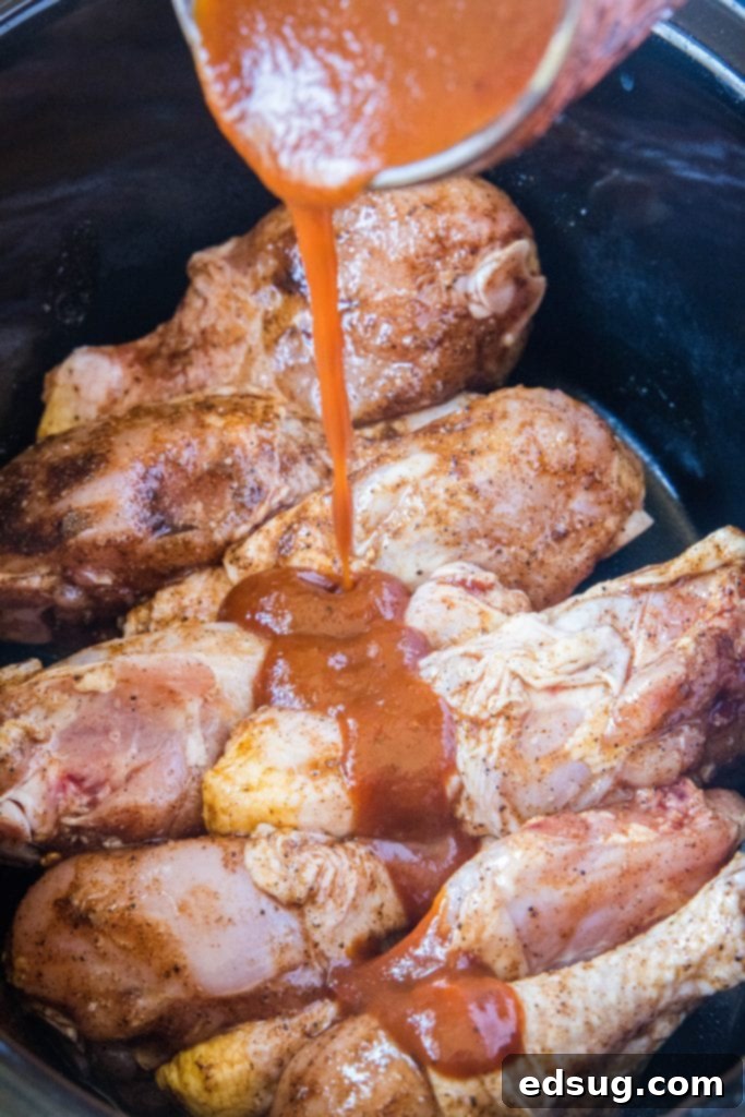 Fall-Off-The-Bone Slow Cooker Drumsticks 5 Pouring a thick layer of barbecue sauce over chicken drumsticks cooking in a crockpot.