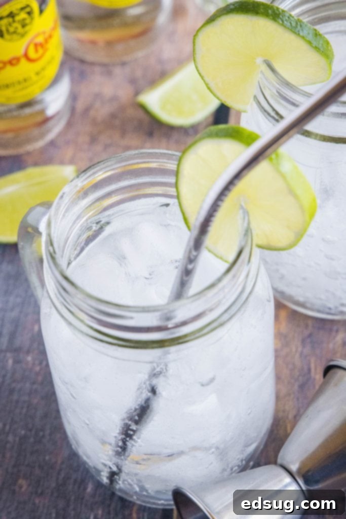 glass of tequila and soda with a straw and lime garnish