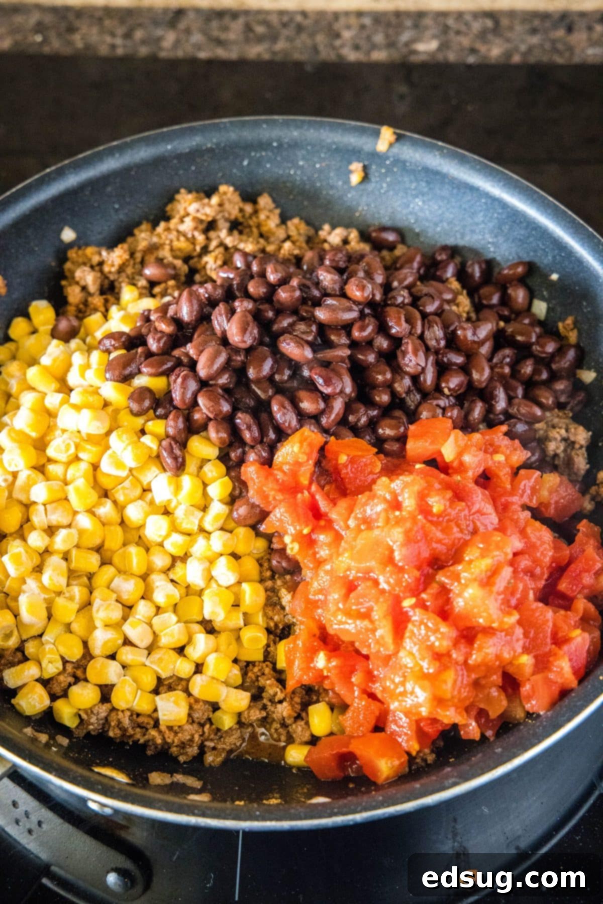 This easy 30-minute taco casserole is loaded with juicy and tender beef, gooey melted cheese, and your favorite taco toppings. A large skillet containing cooked ground beef and onions, mixed with vibrant corn, black beans, and red salsa, all ready to be transferred.
