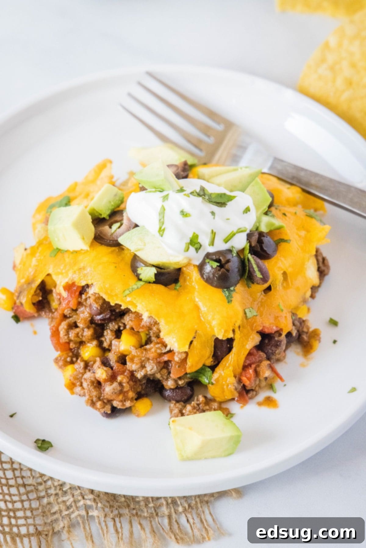 This easy 30-minute taco casserole is loaded with juicy and tender beef, gooey melted cheese, and your favorite taco toppings. An overhead view of a single serving of taco casserole on a plate, with a fork resting beside it, ready to be enjoyed.