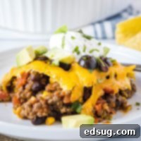 A serving of taco casserole on a plate, topped with sour cream, avocado, cilantro, and olives