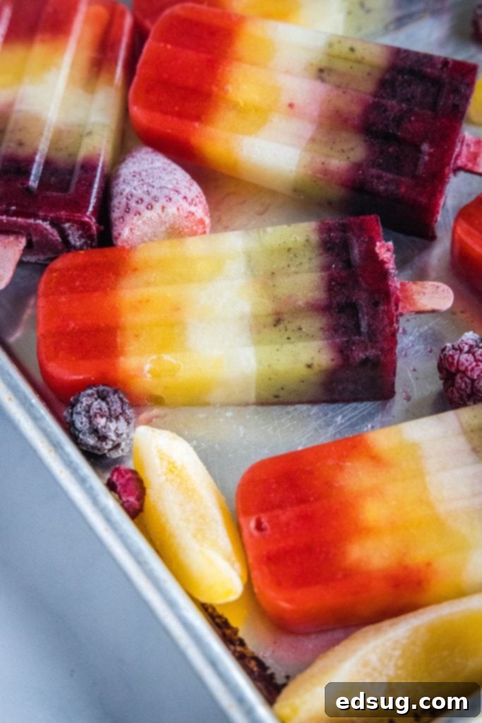 rainbow popsicles on a baking tray next to frozen fruit