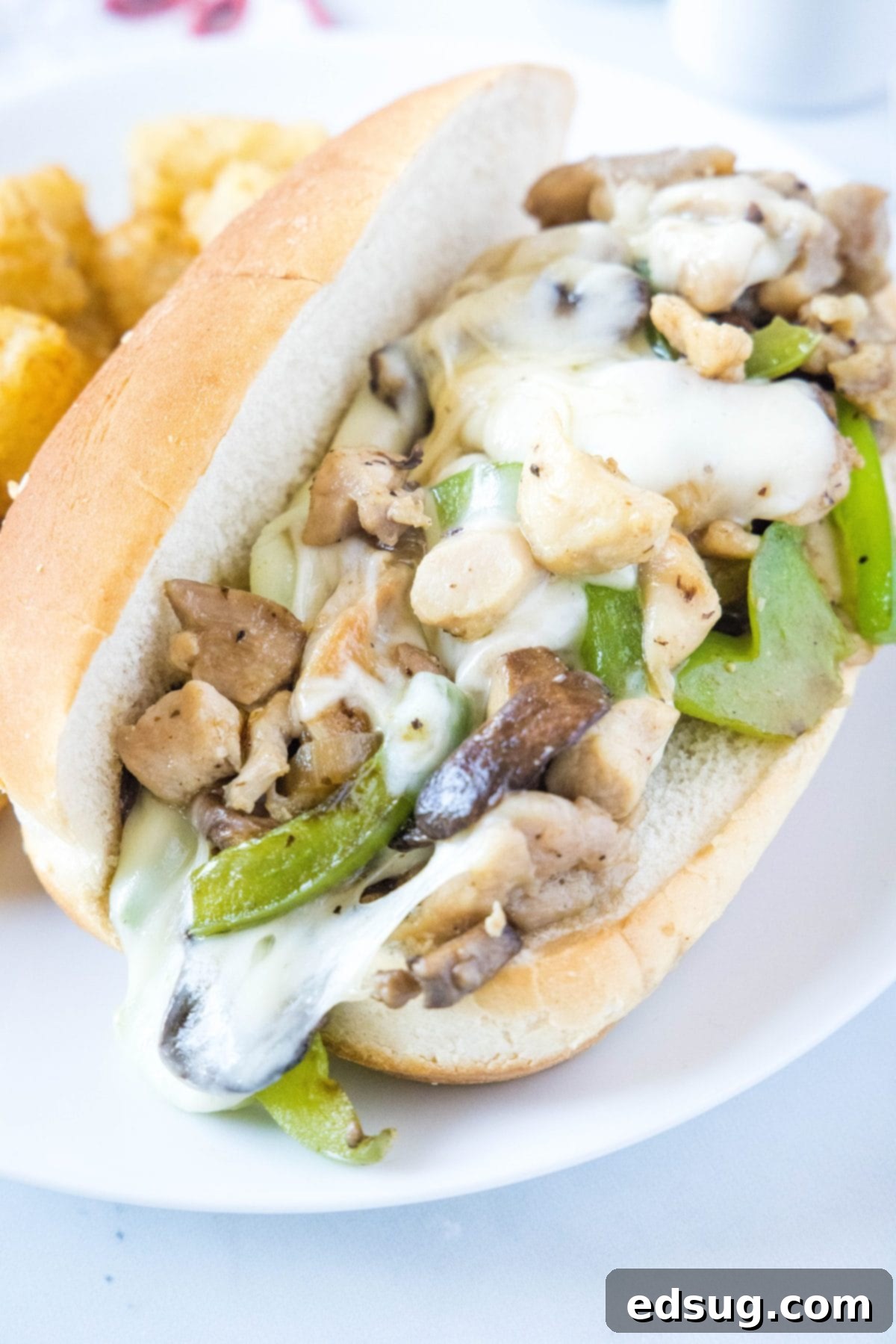 A chicken Philly cheesesteak on a plate with tater tots