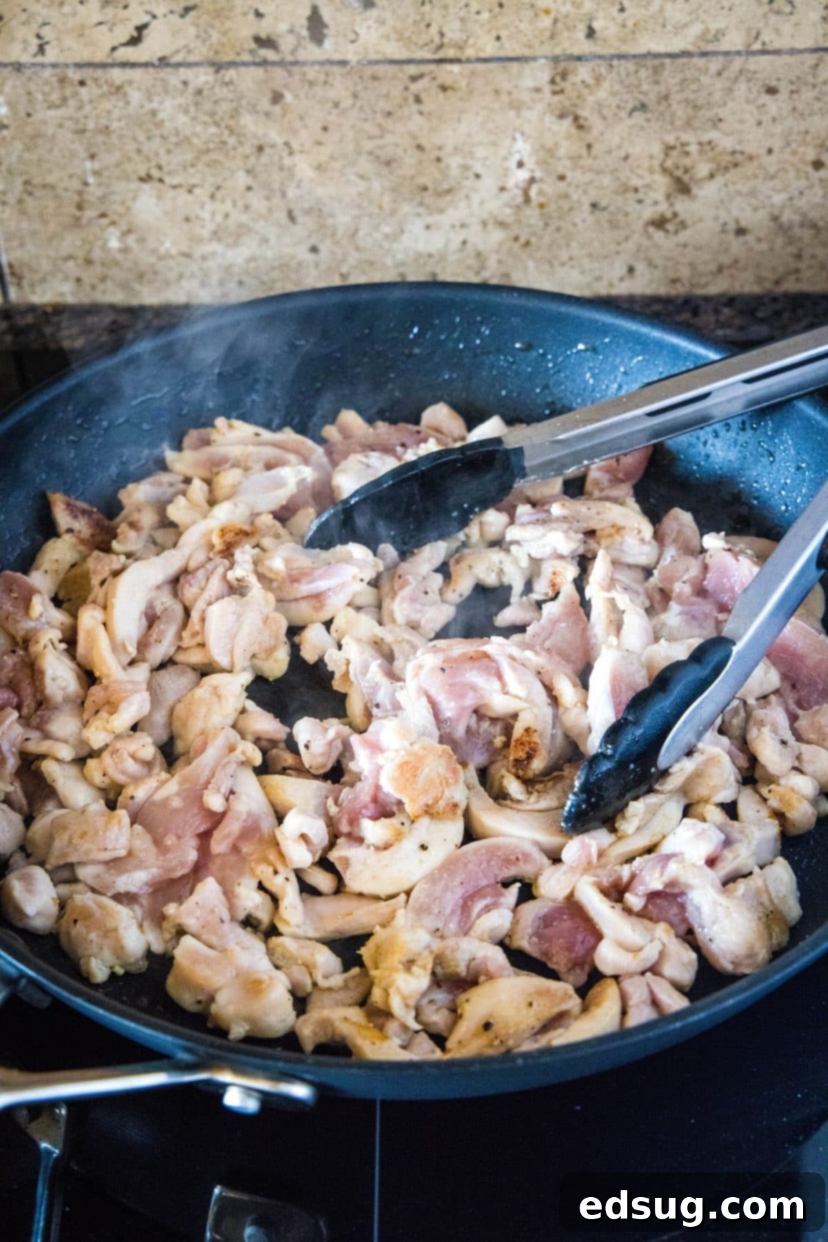 Thin slices of chicken cooking in a skillet, with a pair of tongs