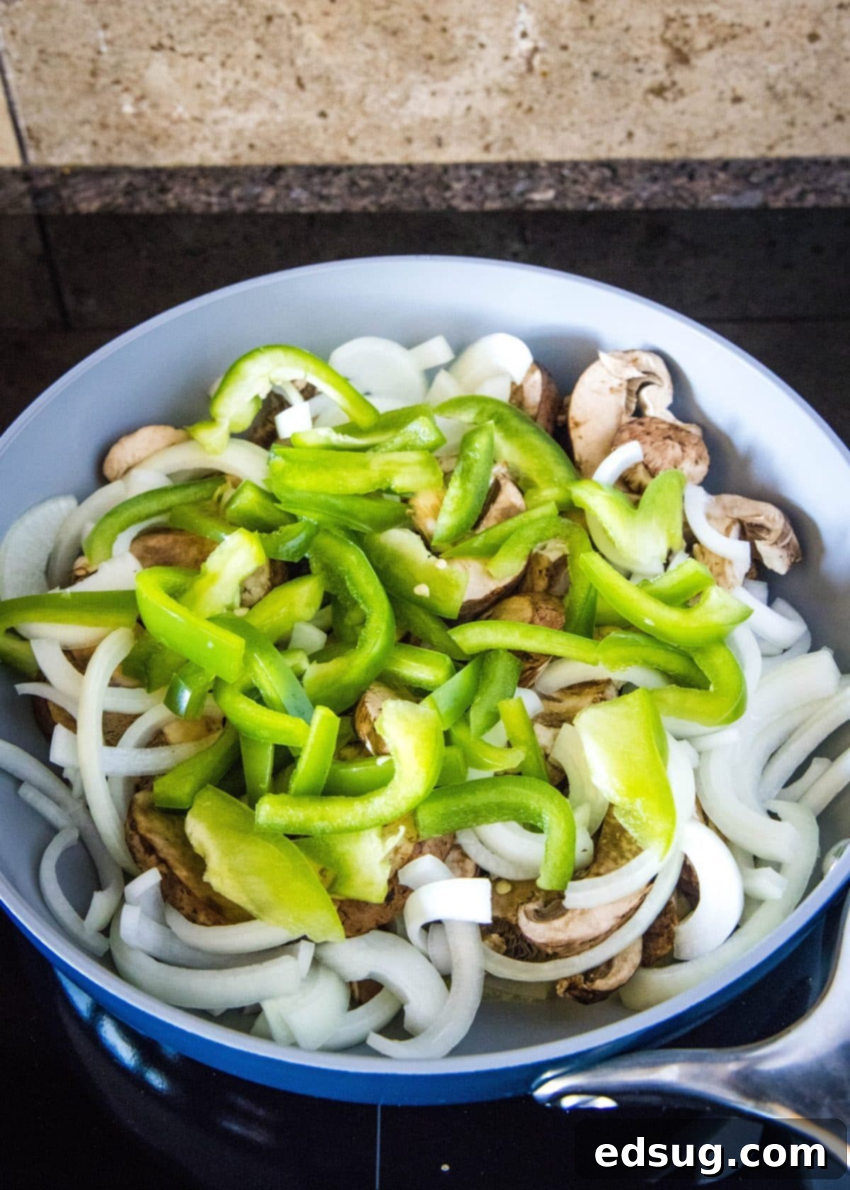A skillet full of uncooked mushrooms, onions, and green bell pepper