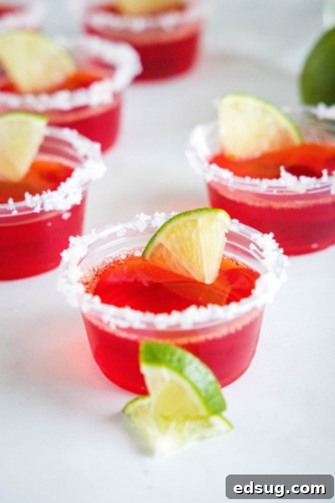 Vibrant strawberry margarita jello shots with lime wedges ready for serving on a rustic table.