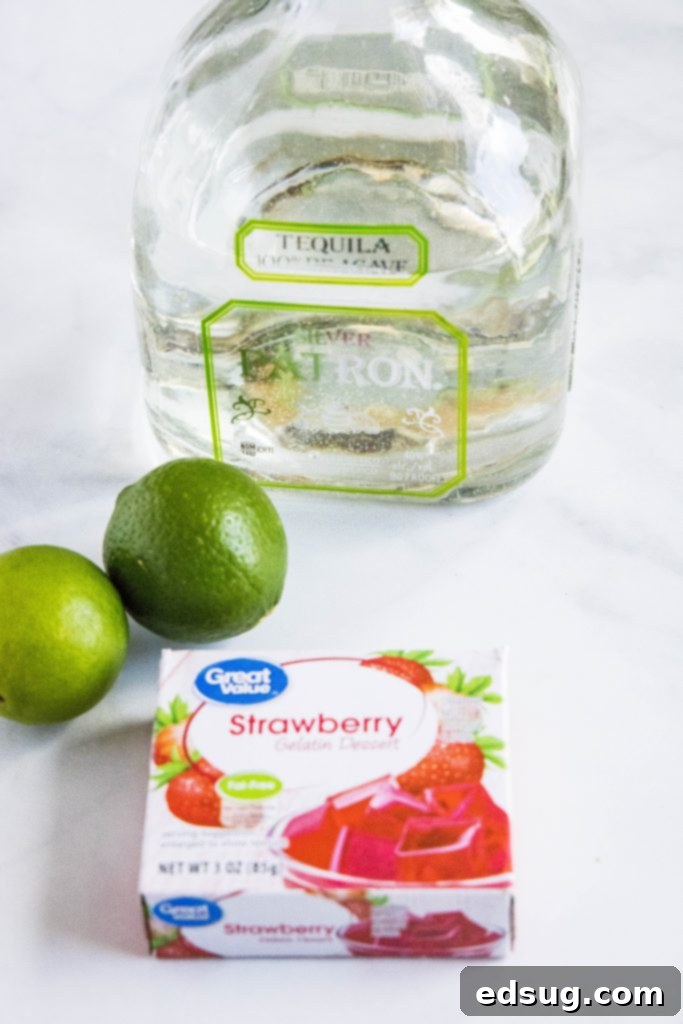 Ingredients for strawberry margarita jello shots laid out on a white surface, including jello mix, limes, tequila, and salt.