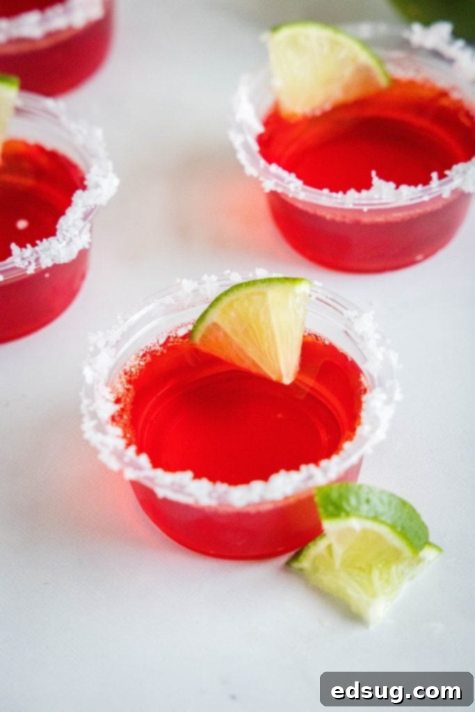A tray of perfectly rimmed and garnished strawberry margarita jello shots arranged on a table for a party.