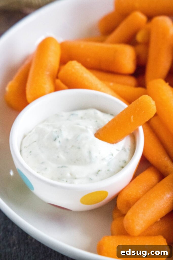 A crisp carrot stick being dipped into a bowl of homemade ranch dressing.