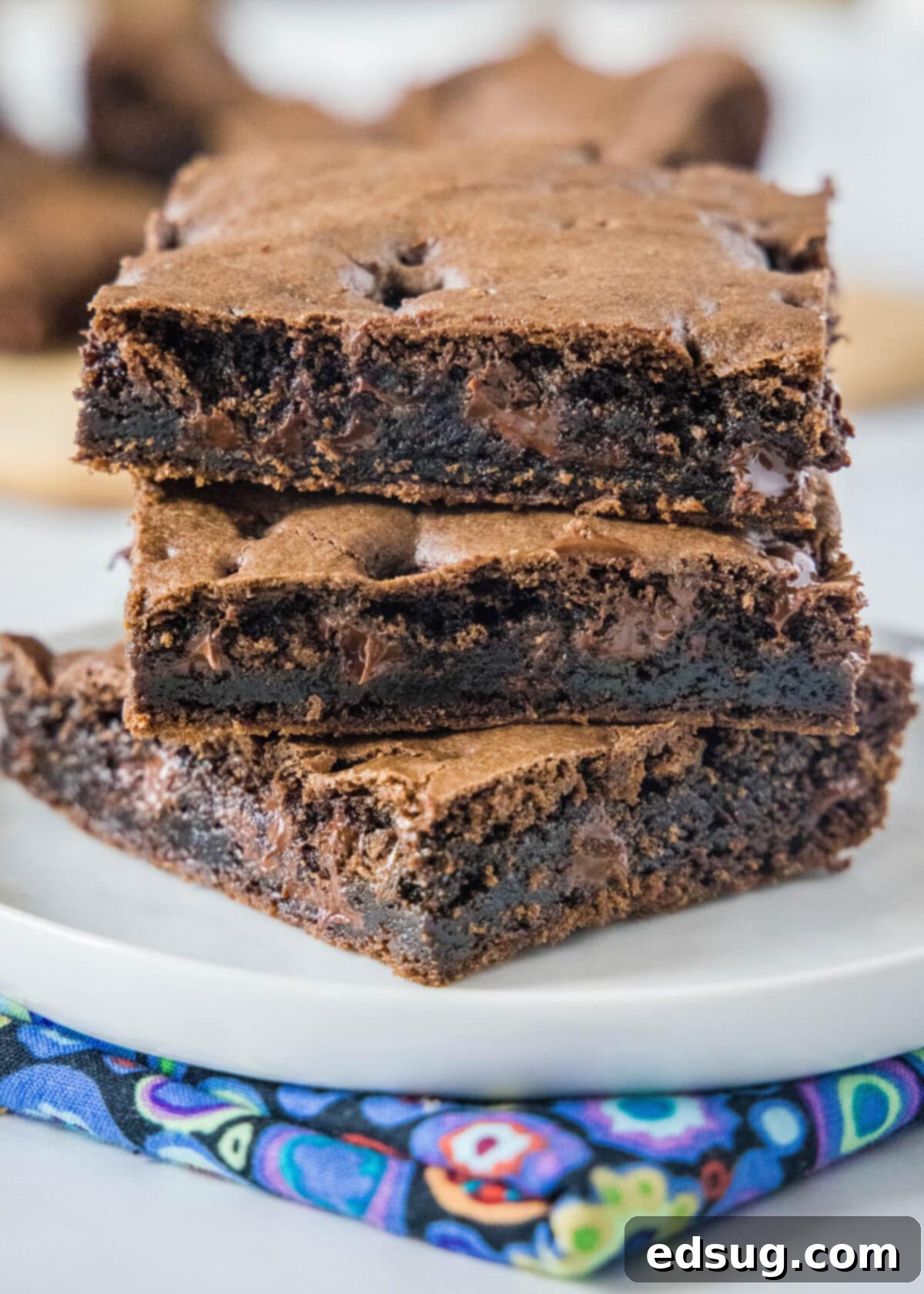 These 30-minute cake mix brownies only use 5 ingredients, and they're moist, soft, and packed full of chocolate flavor Close up of three rich, moist brownie squares stacked on top of each other on a plate, showcasing their decadent texture