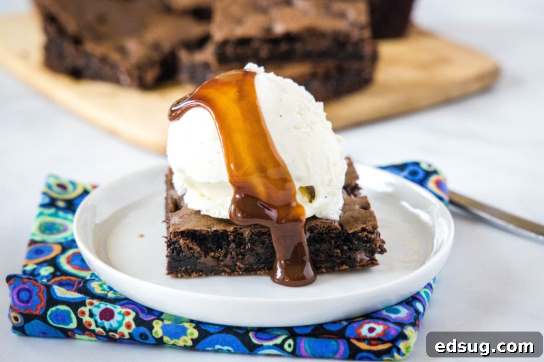 These 30-minute cake mix brownies only use 5 ingredients, and they're moist, soft, and packed full of chocolate flavor A single fudgy brownie square on a plate, topped with a generous scoop of creamy vanilla ice cream and drizzled with luscious chocolate sauce, with more brownies blurred in the background