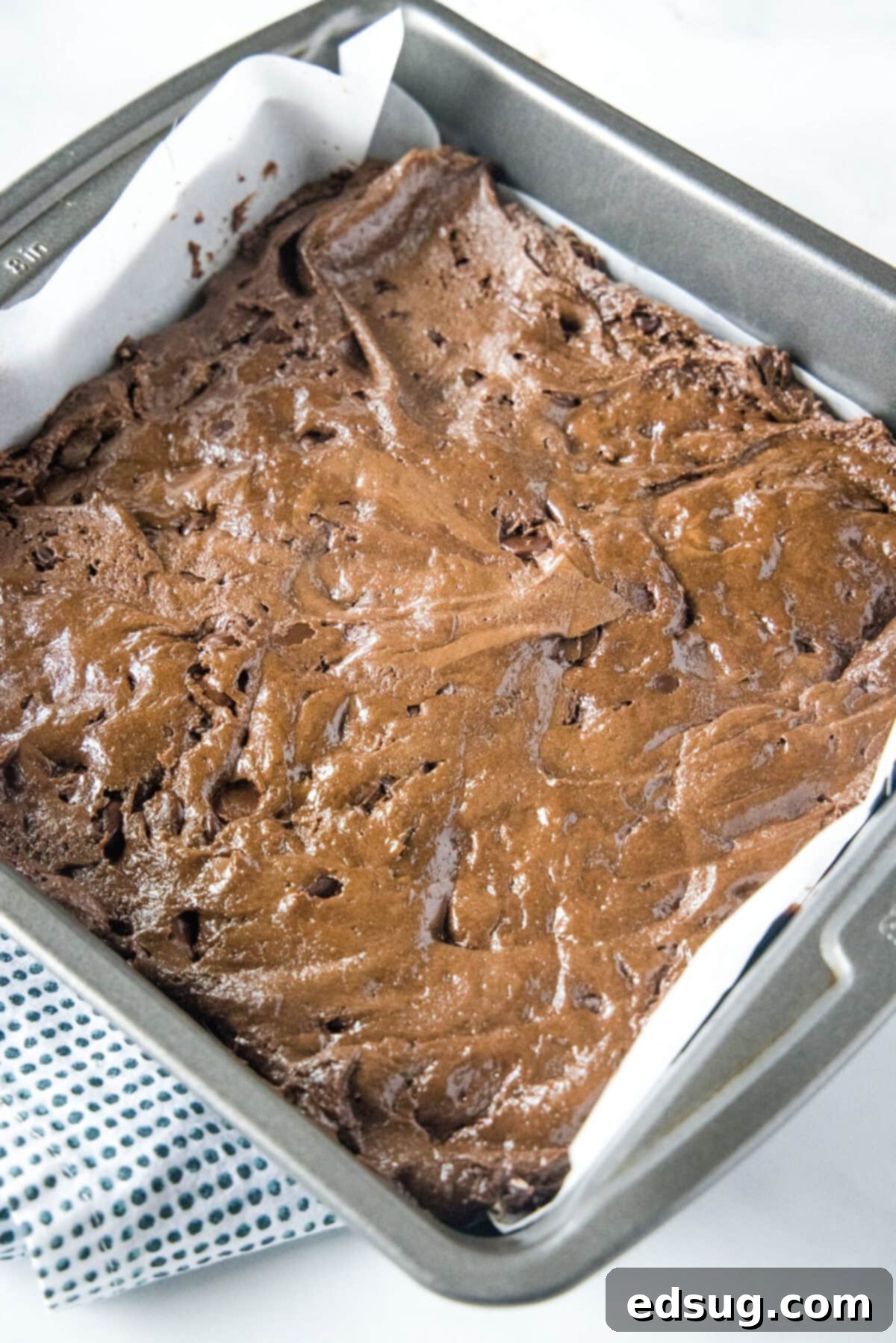 These 30-minute cake mix brownies only use 5 ingredients, and they're moist, soft, and packed full of chocolate flavor Overhead view of a square baking dish, neatly lined with parchment paper, and filled with a smooth, even layer of rich brownie batter, ready to be baked