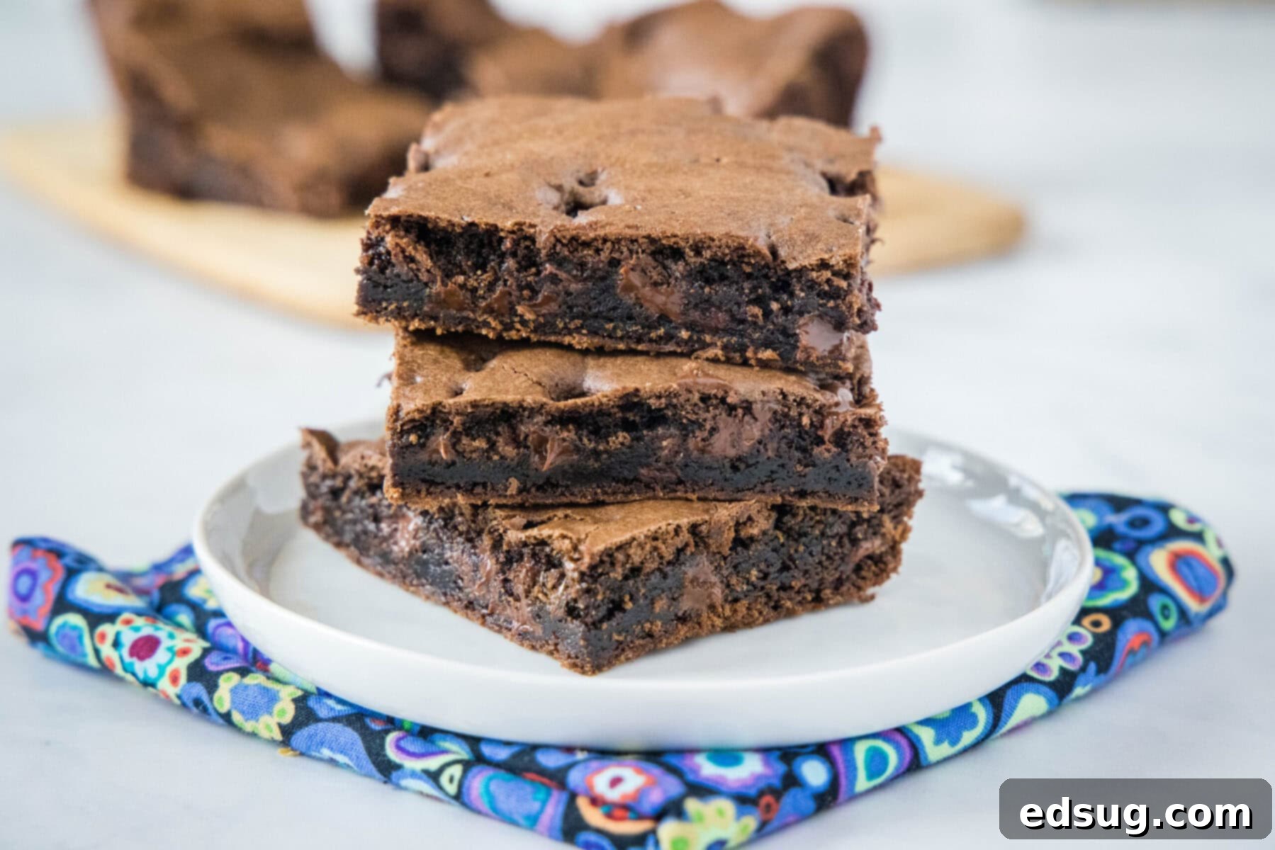 These 30-minute cake mix brownies only use 5 ingredients, and they're moist, soft, and packed full of chocolate flavor A clean white plate holding three perfectly stacked squares of fudgy brownies, showcasing their rich, dark color and inviting texture