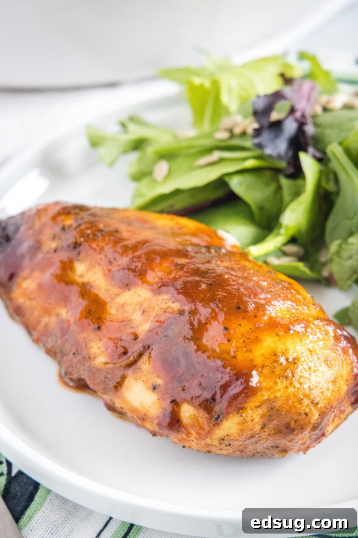 A BBQ chicken breast on a plate with salad, showcasing its golden-brown, saucy exterior and tender texture.