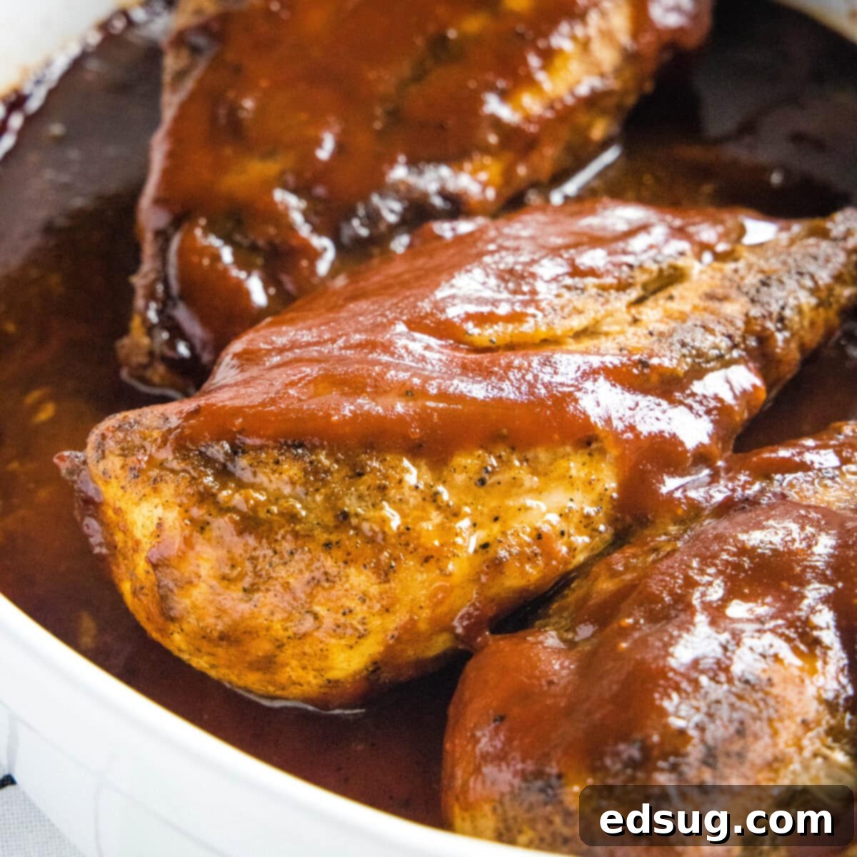 Three chicken breasts covered in rich BBQ sauce, nestled in a baking dish, ready for the oven.