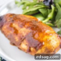 Close up picture of a BBQ chicken breast on a plate next to some salad, garnished and ready to eat.