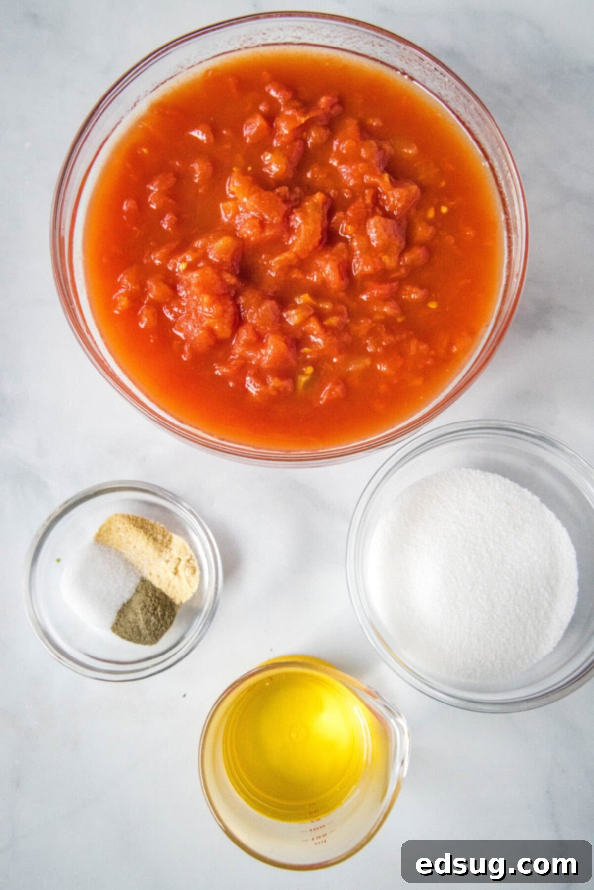 Homemade ketchup is tangy, salty, smooth, and so much better than the store-bought kind. Plus, it's easy to make and takes less than an hour. Overhead view of the simple ingredients needed for homemade ketchup: a bowl of canned tomatoes, a bowl of assorted spices (salt, pepper, onion powder, garlic powder), a bowl of granulated sugar, and a glass of distilled white vinegar.