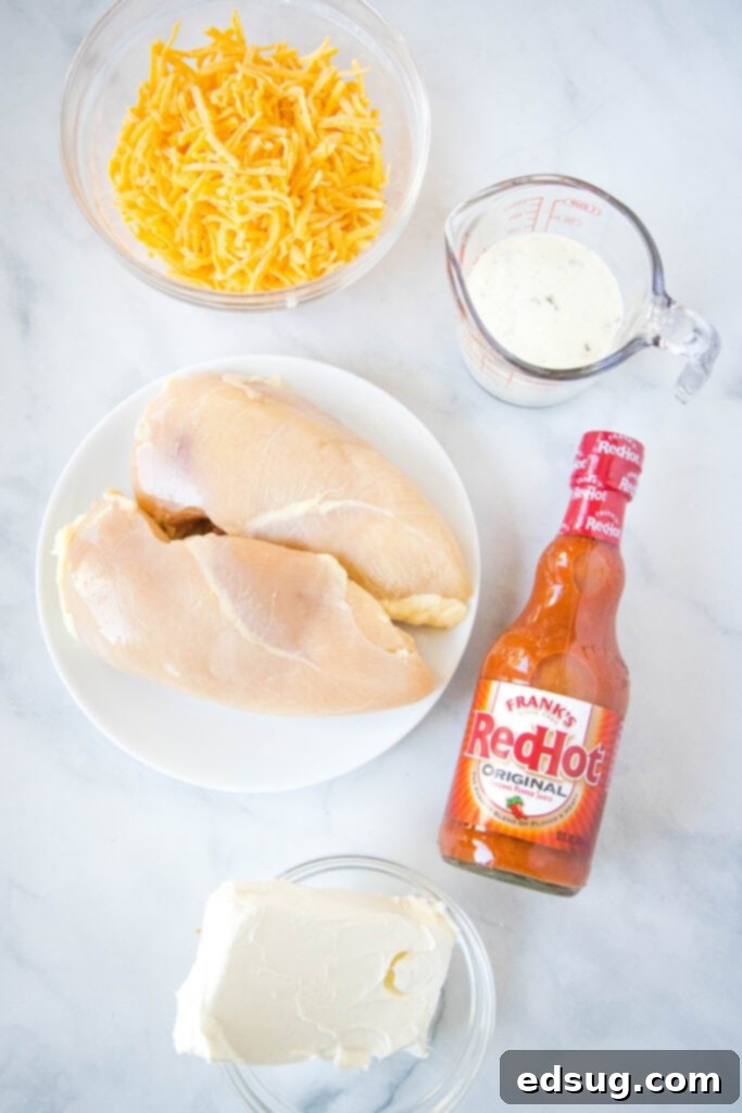 Ultimate Instant Pot Buffalo Chicken Dip 3 close up view of various ingredients for creamy Instant Pot Buffalo Chicken Dip laid out on a rustic wooden surface, including chicken breasts, buffalo sauce, ranch dressing, cheddar cheese, and cream cheese