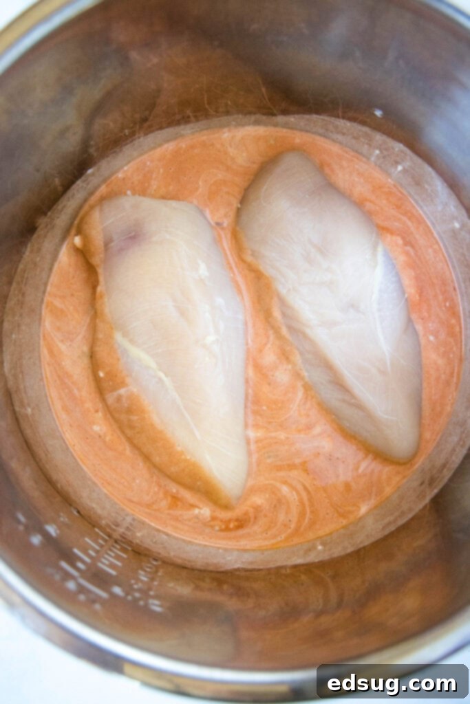 Ultimate Instant Pot Buffalo Chicken Dip 4 raw chicken breasts partially submerged in a vibrant mixture of ranch and buffalo sauce in the Instant Pot liner, ready for pressure cooking