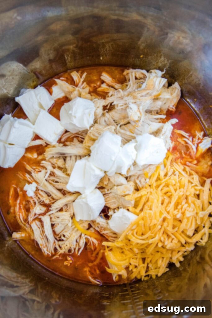 Ultimate Instant Pot Buffalo Chicken Dip 5 adding cream cheese cubes and freshly shredded cheddar cheese to perfectly cooked, shredded chicken in an Instant Pot with buffalo sauce and ranch dressing