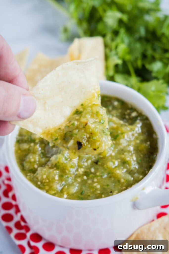 A close-up shot of a hand scooping fresh homemade salsa verde onto a tortilla chip, highlighting the vibrant texture and perfect consistency of the dip.