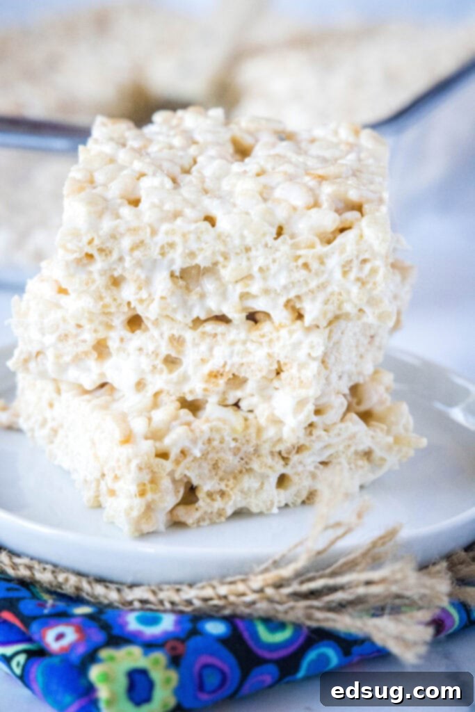 Stacked, perfectly gooey homemade Rice Krispie treats on a pristine white plate, showcasing their irresistible texture and golden hue.