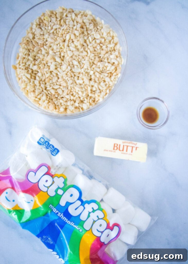Essential ingredients for the best gooey Rice Krispie Treats laid out on a clean surface: Rice Krispies cereal, butter, marshmallows, and vanilla extract.