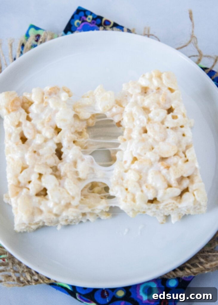 A gooey Rice Krispie Treat being broken in half, showcasing its stretchy, soft texture.