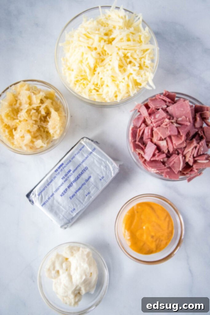 Hot Reuben Dip 3 An array of fresh ingredients for Reuben Dip laid out on a cutting board, including cream cheese, corned beef, Swiss cheese, mayo, Thousand Island dressing, and sauerkraut.