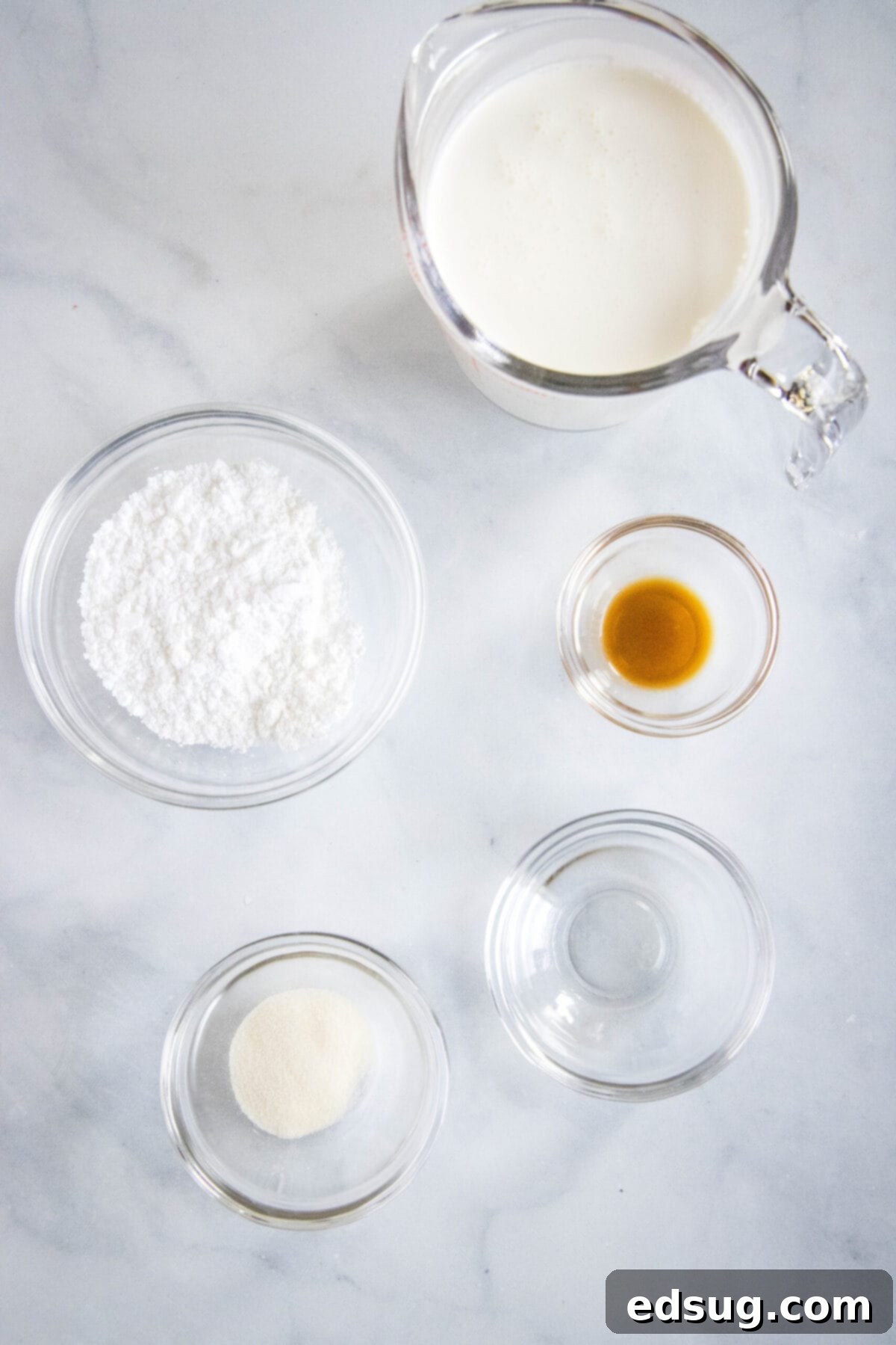 Stabilized Whipped Cream Ingredients Overhead view of the ingredients needed for stabilized whipped cream: a pyrex of whipping cream, a bowl of powdered sugar, a bowl of vanilla extract, a bowl of gelatin powder, and a bowl of water, neatly arranged.