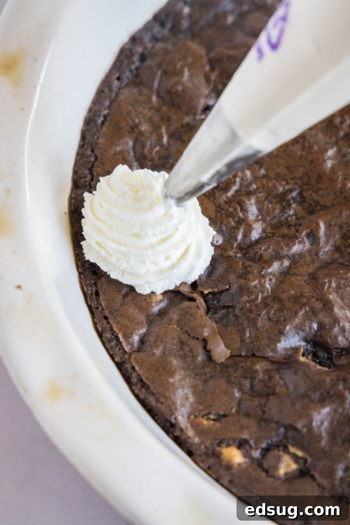 Piping Stabilized Whipped Cream Close up of a piping bag piping cool whip onto a chocolate cake, demonstrating precision and stability.
